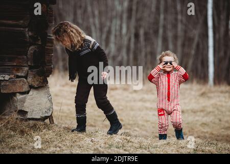Kids walking in forest by wooden house wearing scandinavian onesies Stock Photo