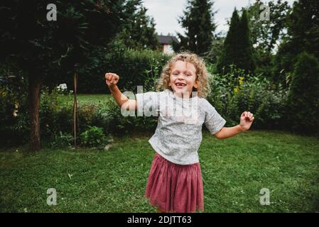 Adorable girl smiling and jumping in garden missing two front teeth Stock Photo