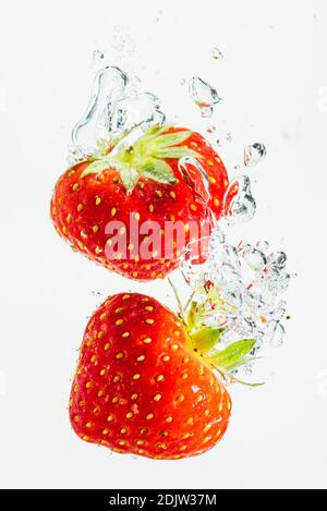 Strawberry falls deeply under water with a big splash. Fruit sinking in clear water on white background. Antioxidant concept Stock Photo