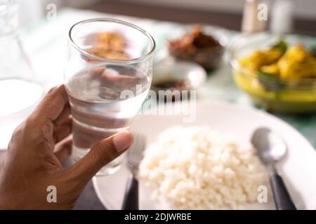 Hand holding a glass of water with indonesian food background Stock Photo