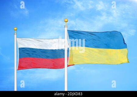Russia and Ukraine two flags on flagpoles and blue cloudy sky Stock Photo