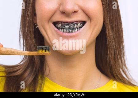 Closeup of smiling woman brushing teeth with black charcoal whitening toothpaste Stock Photo