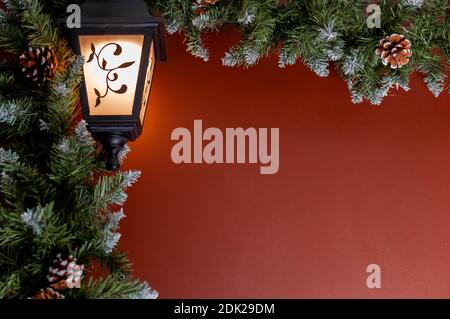 Luminous lantern, Christmas garland with green fir branches and cones on the background of a red wall with space for text. Shallow depth of field and Stock Photo