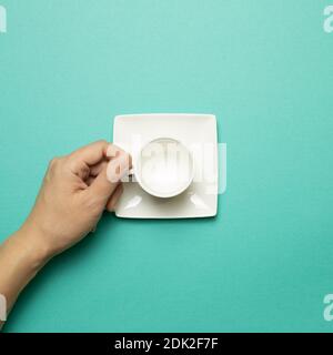 Female hand holding white empty mug cup on mint green background. top view Stock Photo