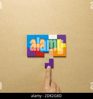 Set of color blocks puzzle pieces and hand holding last one piece on brown background. Creative thinking, idea, problem solving, success concept. top Stock Photo