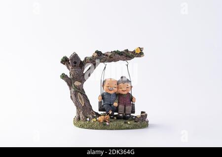 A cute decoration with figures of an elderly cute couple sitting happily on the swing under the tree Stock Photo