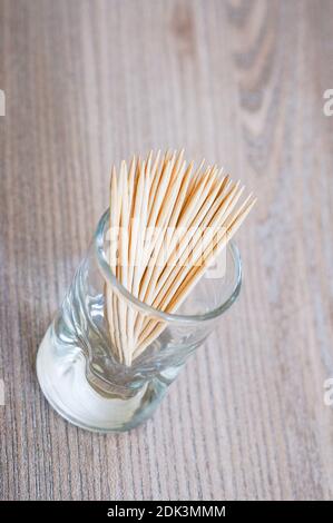 A vertical shot of toothpicks in a shot glass, on a wooden surface Stock Photo