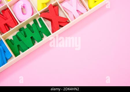 A top view of colorful wooden letters in their case, placed on a pink surface Stock Photo