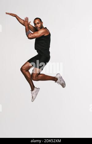 Portrait of african american athlete jumping in air. Fit man doing exercise on white background. Stock Photo