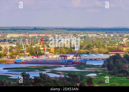 Portal cranes in the small port on a river load barges and cargo ships. Stock Photo