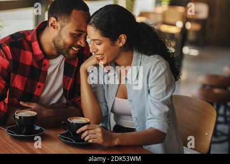 Beautiful couple on a date at cafe. Man and woman sitting at coffee shop table with two cups of coffee talking and smiling. Stock Photo