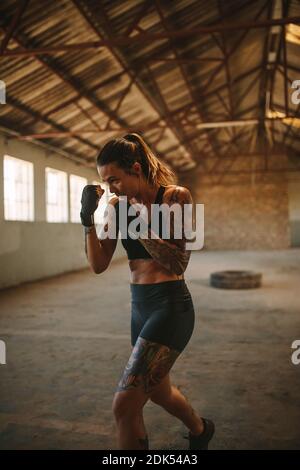 Muscular woman working out in cross training workout space. Fit young female practicing shadowboxing in old empty warehouse. Stock Photo