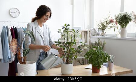 Positive millennial woman office manager starting workday by watering flowers Stock Photo