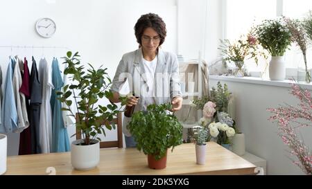 Attentive young female florist enjoying taking care of indoor plants Stock Photo