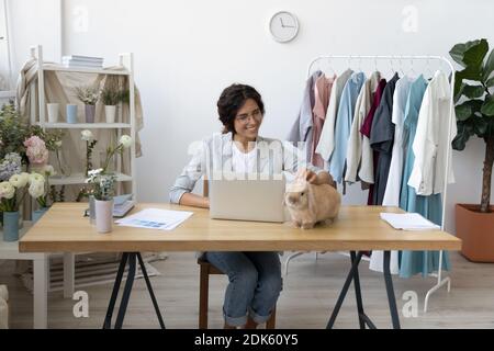 Affectionate woman tailor sitting at studio caressing cute bunny rabbit Stock Photo