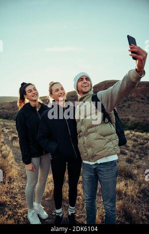 Group of male and female friends hiking in beautiful mountain terrain taking selfies for family  Stock Photo