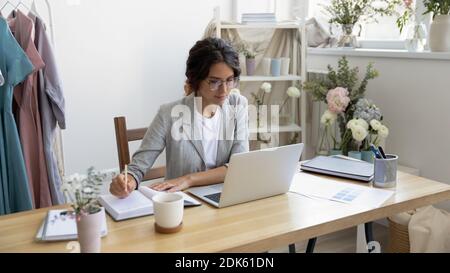 Busy female designer sitting by pc making notes in planner Stock Photo