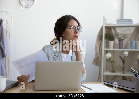 Pensive young woman dressmaker sitting at atelier creating new clothes Stock Photo