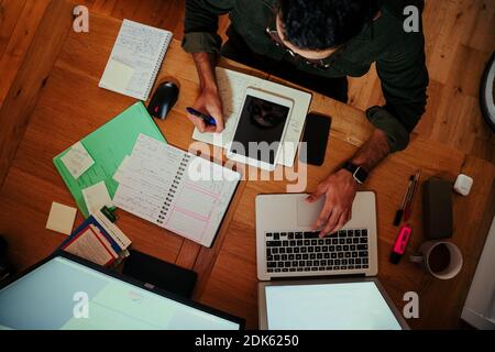 Mixed race working male typing on laptop and writing in notepad busy sitting at office desk  Stock Photo