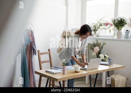 Motivated young female clothing designer standing by laptop printing email Stock Photo