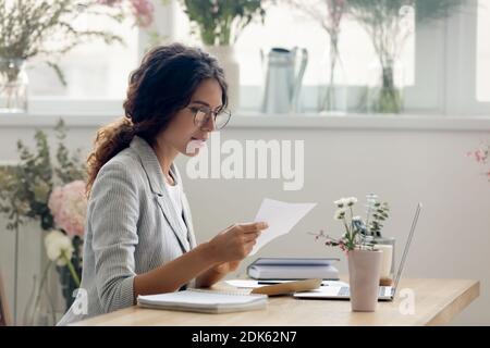 Focused young businesswoman reading paper letter at work desk Stock Photo