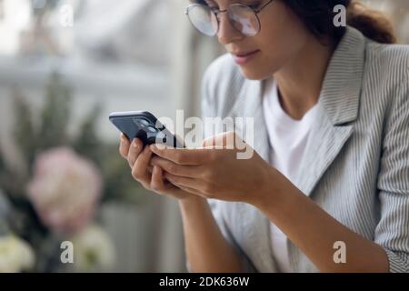 Concentrated millennial female in glasses holding smartphone making answering call Stock Photo