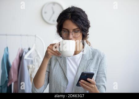 Focused young woman dressmaker drinking coffee answering call by cellphone Stock Photo