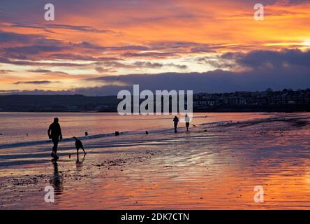 Portobello, Edinburgh, Scotland, UK. 15 December 2020. Fiery sky at sunrise for those walking their dog by the shore of the Firth of Forth. Credit: Arch White/Alamy Live News.