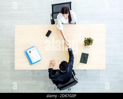 High angle view of businessman in suit shaking hand with woman candidate over wooden desk with resume or cv papers in office. Job interview, business, Stock Photo