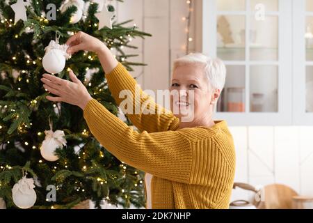 Smiling elderly woman decorating Christmas tree, kitchen interior Stock Photo