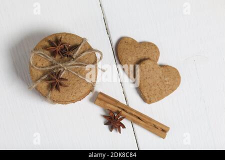 Gingerbread cookies tied with twine. Next to it are cinnamon sticks and anise stars. On boards painted white. Stock Photo