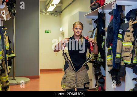 Female firefighter putting protective workwear on in locker room Stock Photo