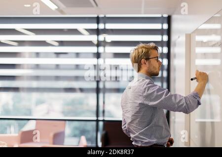 Businessman writing on whiteboard in office Stock Photo