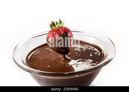 Chocolate dripping from strawberry onto glass cup with melted dark chocolate on white background Stock Photo