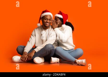Romantic Black Woman Whispering To Boyfriend's Ear, Sharing Christmas Secret