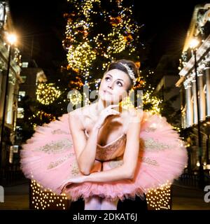 A protrait of a ballet dancer dressed as the Nutcracker's Sugar Plum Fairy sitting in front of a Christmas tree, in Piccadilly, London Stock Photo