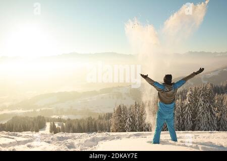 Happy Man standing in deep snow throwing snow into sunrise sunlight. Beautiful Winter Mountain Landscape. Allgau, Bavaria, Alps, Germany. Stock Photo