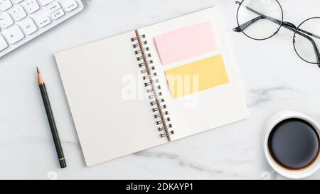 Top view of office table desk cozy work concept with keyboard, notebook, pencil, eyeglasses and coffee on bright marble white background. Stock Photo