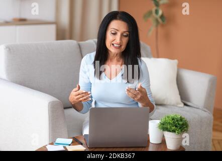 Mature woman sitting on couch, having video call on computer Stock Photo