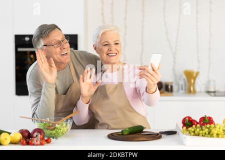 Senior Couple Making Video Call Using Mobile Phone In Kitchen Stock Photo