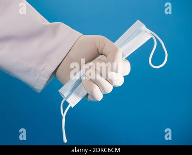 mask in doctor hand with surgical glove and blue background. Stock Photo