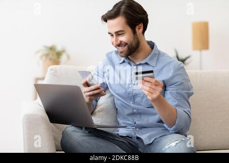 Man Using Phone And Credit Card For Online Shopping Indoor Stock Photo