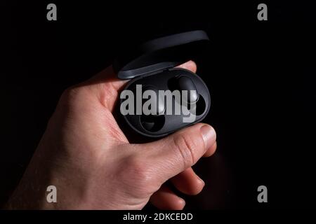 Black wireless headphones in hand, isolated on black background. Stock Photo