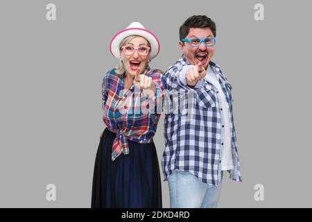 Couple of friends, adult man and woman in casual checkered shirt standing together back to back pointing finger, looking amazed, surprised or laughing Stock Photo
