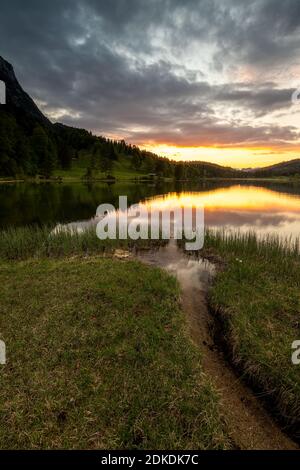 Evening mood at Ferchensee above Mittenwald and below the Wetterstein. A small stream with yellow pollen runs towards the lake and the colors of the sunset. Stock Photo