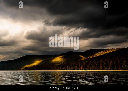 Storm clouds and light mood over Altlach, on the Walchensee in the Bavarian Alps, the Karwendel and Ester Mountains. Intense sunlight illuminates sections of the forest while dark storm clouds shade the rest. Stock Photo