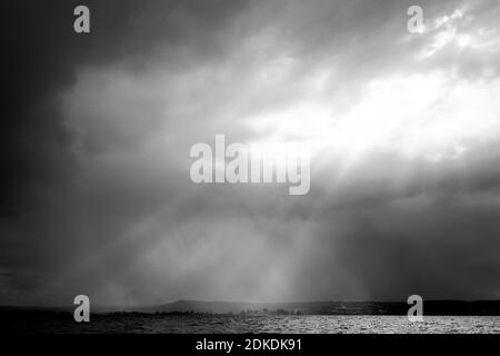 A storm moves over the Ammersee, rays of light from the sun break through the clouds and shine on the opposite shore of the lake. Stock Photo