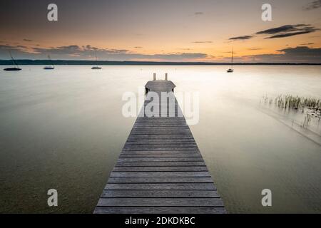 Waves smoothed by long exposure on a boardwalk at Ammersee, in the background the sunset. Stock Photo