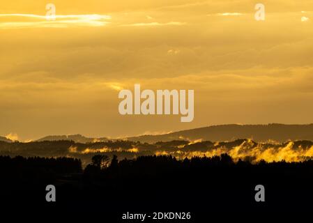 Evening light with clouds and fog in the foothills of the Alps near Murnau. A golden glow over the forest and the hilly landscape. Stock Photo