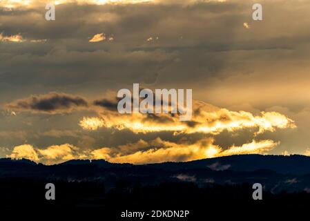 Evening light with clouds and fog in the foothills of the Alps near Murnau. A golden glow over the forest and the hilly landscape. Stock Photo